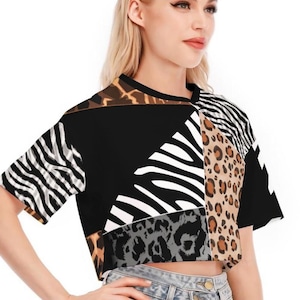 May include: A short-sleeved crop top featuring a patchwork design of various animal prints including black and white zebra stripes, brown leopard spots, and grey cheetah patterns on a black background, paired with light blue denim shorts.