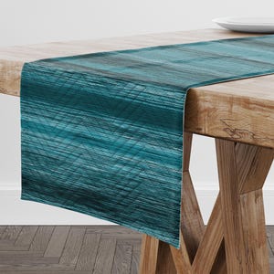 May include: Teal table runner with a subtle geometric pattern. The runner is made of a soft, textured fabric and has a slightly faded look.