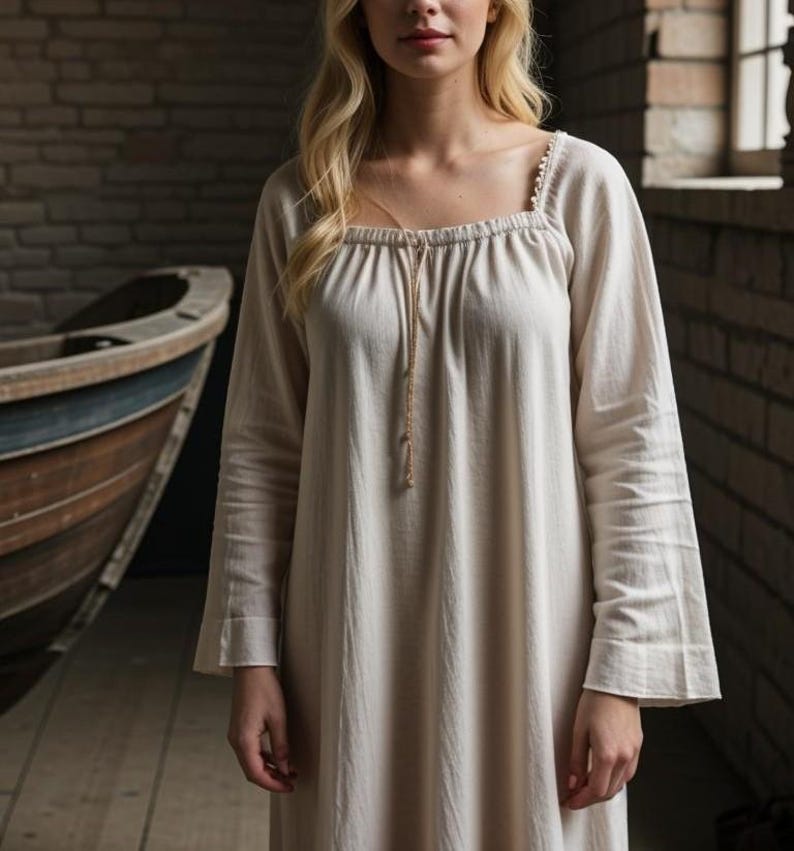 K&ouml;nnte beinhalten: Ein wei&szlig;es, lang&auml;rmeliges Baumwollkleid mit quadratischem Ausschnitt und einem Kordelzug am Hals. Das Kleid hat ein schlichtes, elegantes Design.