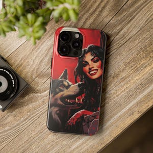 May include: A phone case featuring a woman with long dark hair and a wolf, set against a red background. The artwork has a gothic or fantasy theme. The case is black around the edges and has a glossy finish.