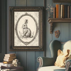 May include: A vintage-style framed print of a black and white illustration of a rabbit sitting in a decorative oval frame. The frame is ornate and has a dark brown finish. The print is on a cream-colored background.