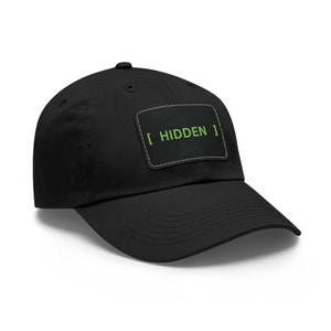 May include: Black baseball cap with a curved brim. A rectangular patch on the front displays the word "HIDDEN" in green, with brackets, and a white border. The cap is made of a soft fabric and has a button on top.