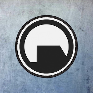 May include: A circular patch featuring a black and white design. The design includes a white semi-circle with a black, right-angled shape at the bottom, all within a black circle. The patch has a black stitched border.