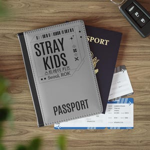 Może przedstawiać: Szary pokrowiec na paszport z napisem "STRAY KIDS" i "스트레이 키즈" w języku koreańskim, a także słowami "Seoul, ROK" i "PASSPORT".