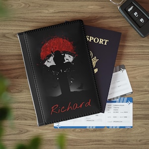 May include: Black passport holder with a red and black graphic of a person standing in front of a red sun. The name "Richard" is printed in red on the front of the holder.