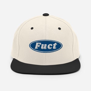 May include: A white and black baseball cap with a blue oval patch that says "FUCT" in white letters.