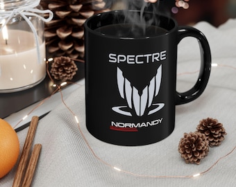 May include: Black ceramic coffee mug with a white graphic of the Spectre logo from the Mass Effect video game series. The logo includes the text "SPECTRE" and "NORMANDY".