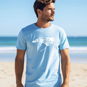 May include: A light blue t-shirt with a white outline of the state of North Carolina and the text "It's Better on Top" printed on the front.
