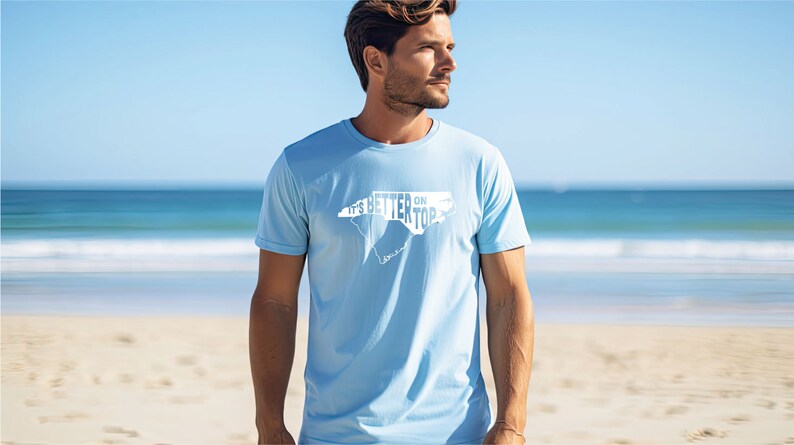 May include: A light blue t-shirt with a white outline of the state of North Carolina and the text "It's Better on Top" printed on the front.