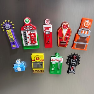 May include: A collection of nine colorful plastic refrigerator magnets shaped like vending machines from the Call of Duty Zombies game, featuring various designs including Quick Revive, Juggernog, Speed Cola, and Stamin-Up with their respective logos.