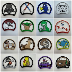 May include: A collection of sixteen circular plastic ear-shaped displays featuring various colorful cartoon and movie character designs, including Darth Vader, lightsabers, Dory, a Stormtrooper, Jessie, Grogu, Rex, Forky, Slinky Dog, Bullseye, Woody, Genie, Mickey Mouse, Winnie the Pooh, Zurg, and Mater.