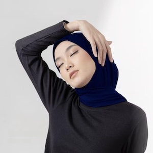 Könnte beinhalten: Ein marineblauer Hijab wird mit einem dunkelgrauen Langarmshirt getragen. Die Augen der Person sind geschlossen und der Arm ist über dem Kopf erhoben. Traditionelles Kleidungsstück.