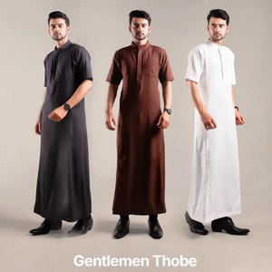 May include: Three thobes in black, brown, and white. Each thobe has short sleeves, a mandarin collar, and a front pocket. The image includes the text "Gentlemen Thobe".