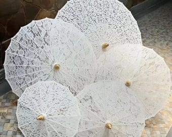 May include: A collection of five white lace parasols, each with a wooden handle and a delicate, openwork design. The parasols are arranged in a visually appealing display, showcasing their intricate patterns and textures. The overall aesthetic is elegant and romantic.
