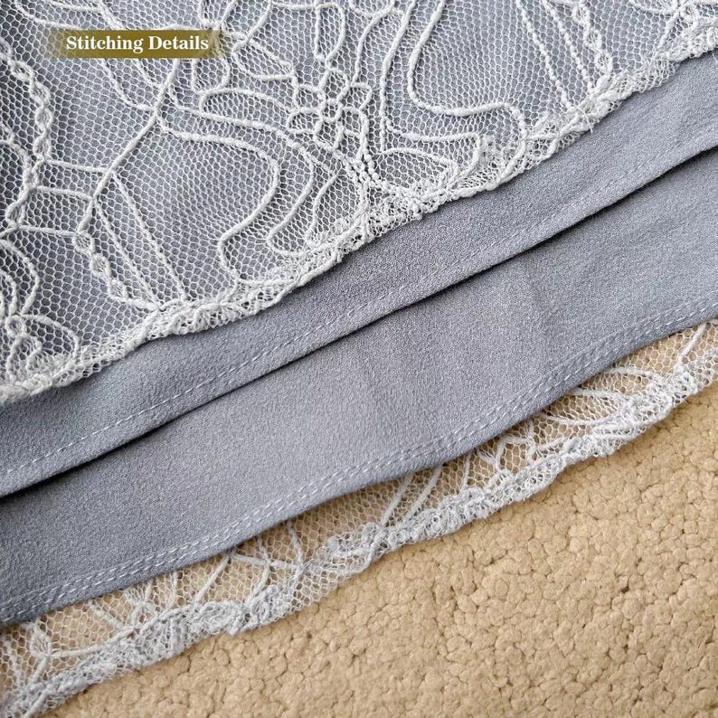 Op de afbeelding: Close-up van een lichtgrijze stof met een witte kantversiering. De stof is dubbelgevouwen en de stikdetails zijn zichtbaar. De tekst "Stitching Details" is zichtbaar in de linkerbovenhoek van de afbeelding.