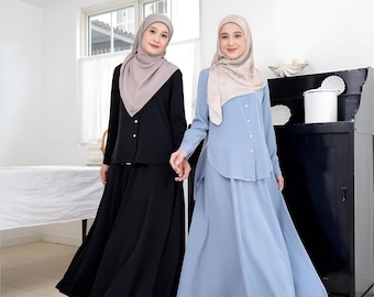 Puede incluir: Dos mujeres con camisas de manga larga y faldas largas. La mujer de la izquierda lleva una camisa y una falda negras, mientras que la mujer de la derecha lleva una camisa y una falda azul claro. Ambas mujeres llevan pañuelos en la cabeza.