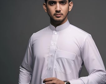 Può includere: Una camicia bianca a maniche lunghe con collo alla coreana e tasca sul petto. La camicia è abbottonata sul davanti. Un orologio da polso nero e oro è visibile al polso.