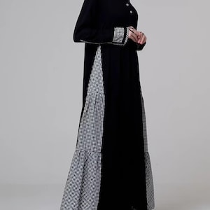 May include: A long black dress with long sleeves and a high neckline. The dress features a contrasting panel of black and white checkered fabric down the front and on the cuffs. The dress has a flowing, modest design.