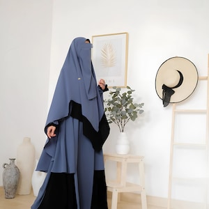 Peut inclure: Une abaya bleue et noire avec une longue jupe fluide et un niqab. L'abaya a un motif décoratif sur la poitrine et une bordure noire autour des bords.