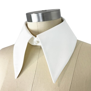 May include: A white detachable collar with pointed edges. The collar is made of a smooth fabric and has a button closure.