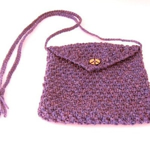 May include: Purple crocheted purse with a flap closure and a peace sign button. The purse has a long strap for carrying over the shoulder.