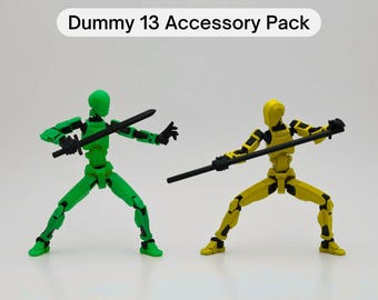 May include: Two articulated action figures, one green and one yellow, holding weapons. The green figure is holding a sword and the yellow figure is holding a staff. The text "Dummy 13 Accessory Pack" is displayed above the figures.