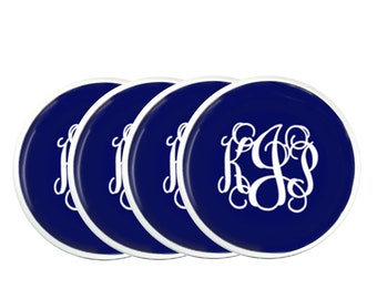 May include: Four navy blue coasters with a white monogram design. Each coaster has a white border and a glossy finish. The monogram features the letters KGS in a decorative script.
