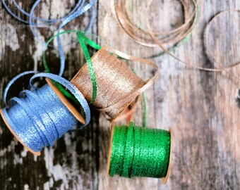 May include: Three spools of ribbon with glitter. The ribbon colors are blue, gold, and green.