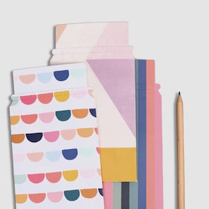 Op de afbeelding: Een verzameling kleurrijke papieren cadeaulabels in de vorm van potten met een houten potlood. De labels hebben verschillende geometrische patronen en pastelkleuren, waaronder roze, blauw, geel en oranje. Het potlood staat verticaal.