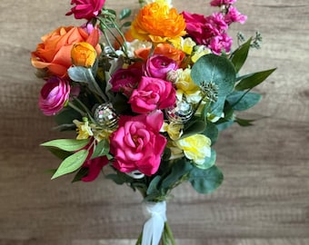 May include: A vibrant bouquet of pink, orange, and yellow flowers with silver accents. The bouquet is tied with a white ribbon and is sitting on a white pedestal.