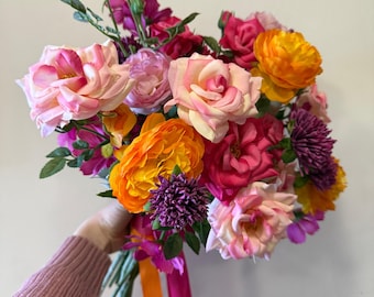 May include: A vibrant bouquet of pink, orange, and purple flowers tied with orange and pink ribbons. The bouquet includes roses, carnations, and other blooms.