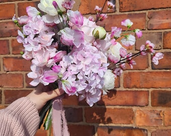 May include: A bouquet of pink and white flowers, including hydrangeas, roses, and cherry blossoms, tied with a pink ribbon.