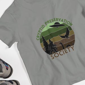 Cryptid Preservation Society Jugend Kurzarm T-Shirt, Jungen, Mädchen, Cryptid, Bigfoot, Mothman, Monster von Loch Ness, Aliens, UFO, Kreaturen