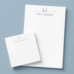 May include: A white rectangular notepad and a smaller white square notepad, both featuring dark blue printed text. The larger notepad displays the initials KH and the name KATE HALBERG, while the smaller notepad shows the initials TW and TENLEY WILKES.