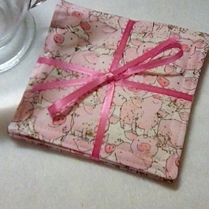 May include: Set of four pink and white fabric coasters with a pig pattern and a pink ribbon tied around them.