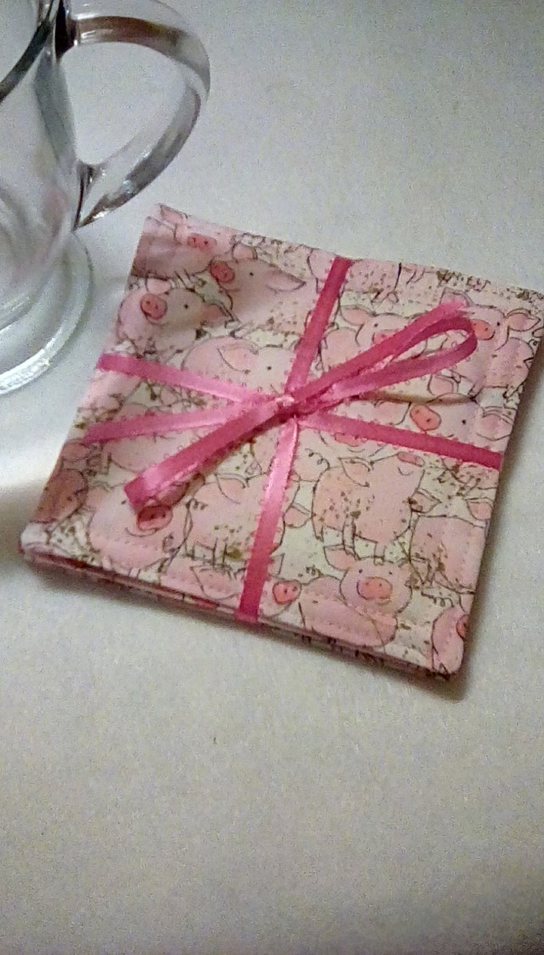 May include: Set of four pink and white fabric coasters with a pig pattern and a pink ribbon tied around them.