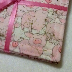 May include: A pink fabric gift bag with a pink satin ribbon tied around it. The bag is decorated with a pattern of pink pigs.