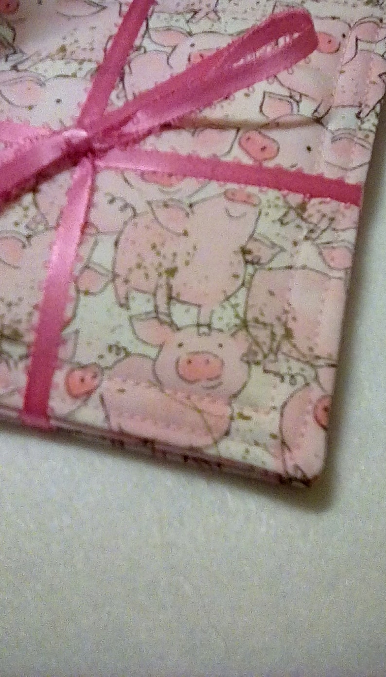May include: A pink fabric gift bag with a pink satin ribbon tied around it. The bag is decorated with a pattern of pink pigs.