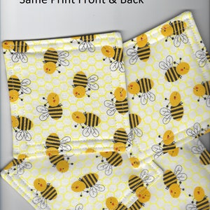 May include: Set of four yellow and black bee-themed fabric coasters. The coasters have a white background with a yellow honeycomb pattern and black and yellow bees.