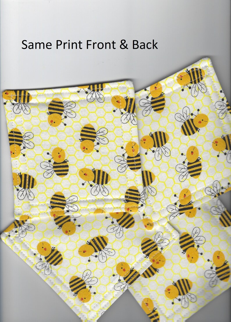 May include: Set of four yellow and black bee-themed fabric coasters. The coasters have a white background with a yellow honeycomb pattern and black and yellow bees.