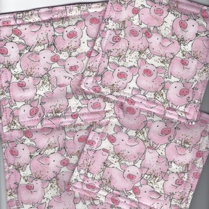 May include: Four pink fabric coasters with a white background and a repeating pattern of pink pigs. The coasters are stitched with a white thread and have a subtle gold glitter effect.
