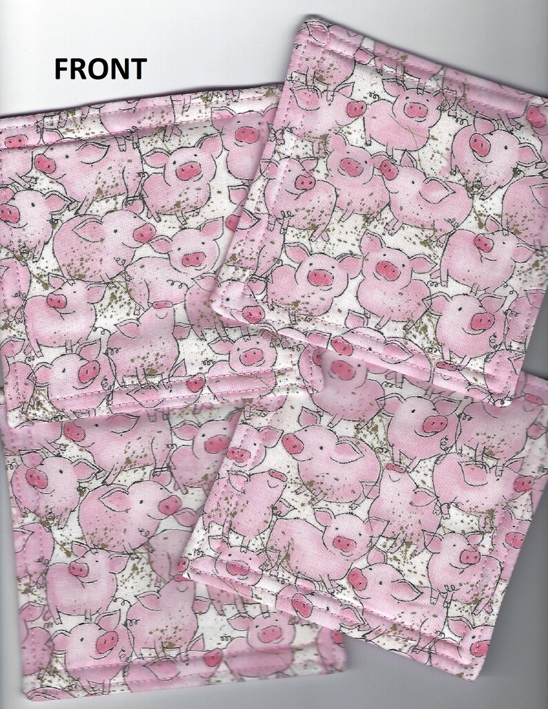 May include: Four pink fabric coasters with a white background and a repeating pattern of pink pigs. The coasters are stitched with a white thread and have a subtle gold glitter effect.