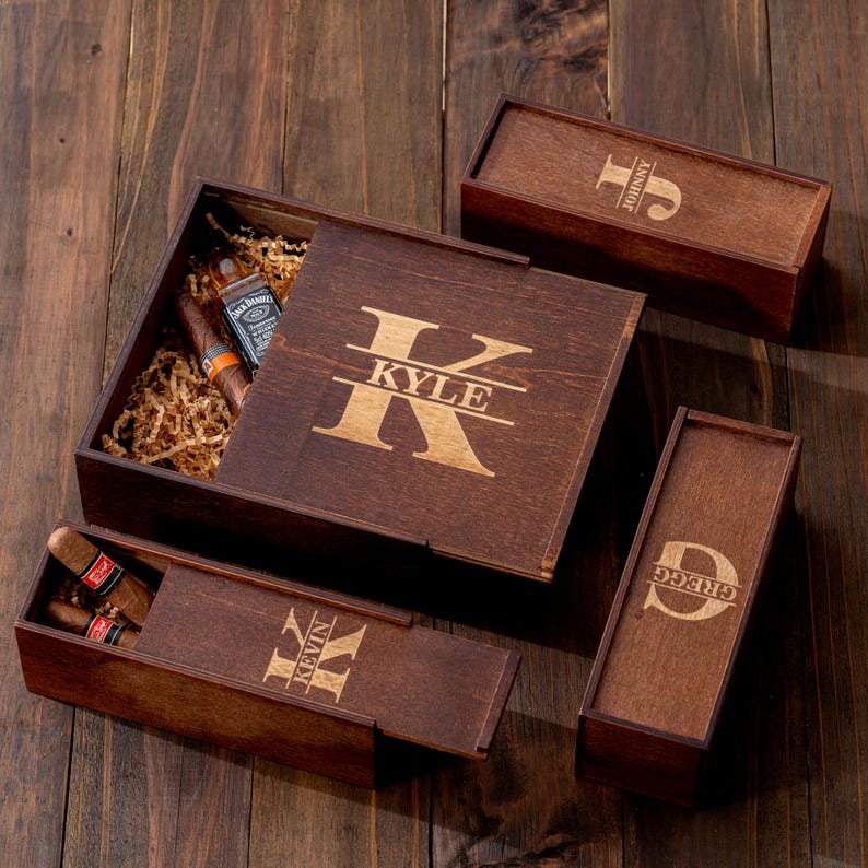 May include: A wooden gift set with a large box and three smaller boxes. The large box has the name "Kyle" engraved on the lid. The smaller boxes are engraved with the names "Johnny", "Kevin", and "Gregg". The large box contains cigars and a small bottle.