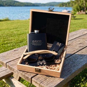 Può includere: Confezione regalo in legno con una fiaschetta nera, occhiali da sole e un porta carte. La fiaschetta è incisa con "DAVID" e "GROOMSMAN 5-10-2025". Gli occhiali da sole hanno montatura in legno. Il porta carte e l'astuccio degli occhiali da sole sono neri.