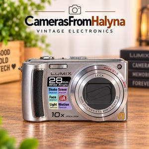 Può includere: Una fotocamera digitale Panasonic Lumix color argento con obiettivo Leica, zoom ottico 10x e grandangolo 28mm. La parte anteriore mostra testo tra cui Mega O.I.S., Shake Detection, Face Detection, Light Detection, Scene Detection e Motion Detection.
