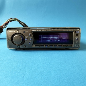 Könnte beinhalten: Ein graues Sony Xplod Autoradio mit einem digitalen Display, das einen Musik-Equalizer, Titelnummer 001 und die Zeit 1:31 anzeigt. Das Gerät verfügt über einen großen runden Lautstärkeregler, mehrere Bedientasten und einen Kabelbaum an der Rückseite.