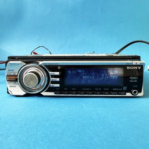 May include: A Sony Xplod car stereo unit with a silver fascia, black buttons, and a digital display. The display shows the time and CD information. The stereo has a large central knob and various function buttons.
