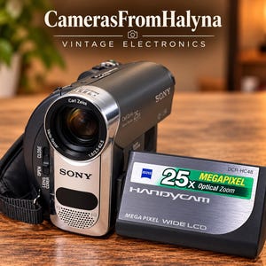 May include: A black Sony Handycam DCR-HC48 camcorder with a silver Carl Zeiss Vario-Tessar lens. The device features a flip-out wide LCD screen displaying 25x Optical Zoom and Mega Pixel text. The camera body includes a lens cover switch and strap.