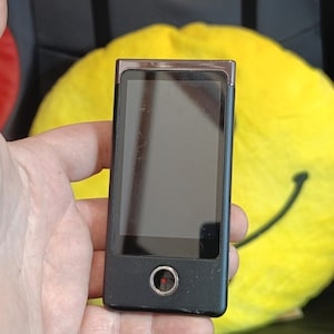 Può includere: Un registratore vocale digitale nero e argento con un piccolo punto rosso sul davanti.