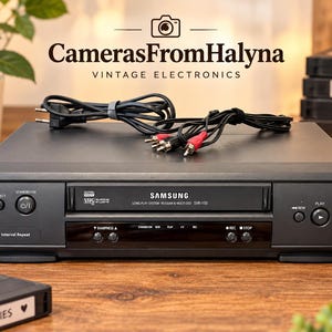 Peut inclure: Un lecteur VHS Samsung SVR-750 noir doté d'une fente de chargement frontale, d'un bouton d'alimentation, d'un bouton d'éjection et de commandes de lecture incluant lecture, rembobinage, avance rapide et enregistrement, avec câbles inclus.